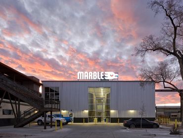 Marble Brewing production facility at sunset with glass facade showcasing brewing equipment inside.