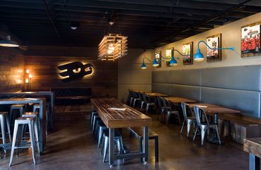 Marble Brewing taproom with wood tables, metal stools, and illuminated Marble logo on feature wall.