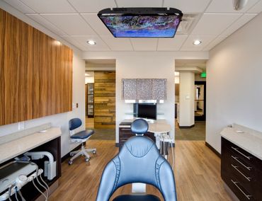 Modern dental exam room with wood finishes, ergonomic seating, and ceiling-mounted screen.