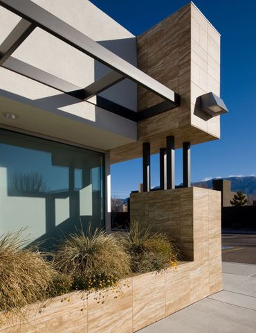 Close-up of modern stone and steel architectural detail with textured landscaping and strong shadows