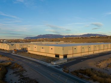 Aerial view of a large industrial warehouse with clean geometry and mountain backdrop at sunrise.