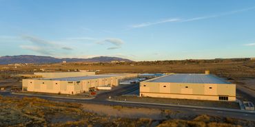 Two modern warehouse buildings in an industrial park with mountain views under clear blue skies.
