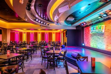 Colorful stage and dining area at Quezada’s Comedy Club with curved ceiling and bold lighting.