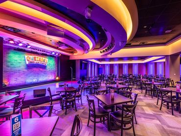 Quezada’s Comedy Club and Cantina interior with stage lighting, seating, and curved ceiling design.