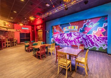 Colorful dining area at Quezada’s Comedy Club and Cantina with mural, bold lighting, and seating.