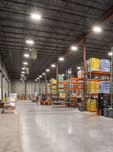 Spacious warehouse interior with tall steel shelving and forklifts under high industrial lighting.