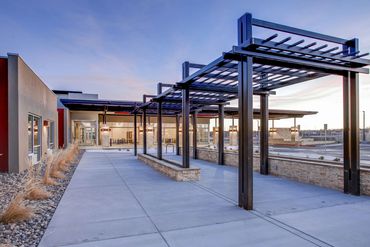 Steel pergola walkway with stone planters and desert landscaping at a senior care facility.