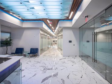 Modern office hallway with marble flooring, glass walls, and geometric ceiling lighting design.