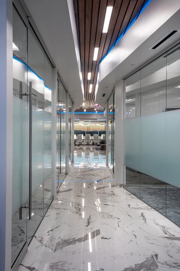 Glass corridor at SC3 HQ with marble floors, wood slat ceiling, and linear LED lighting.