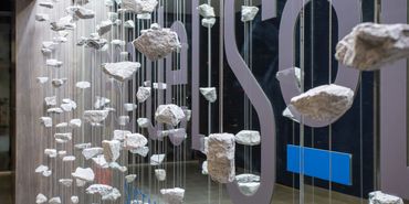 Suspended stone art installation with rocks hanging on wires inside SC3 International headquarters.
