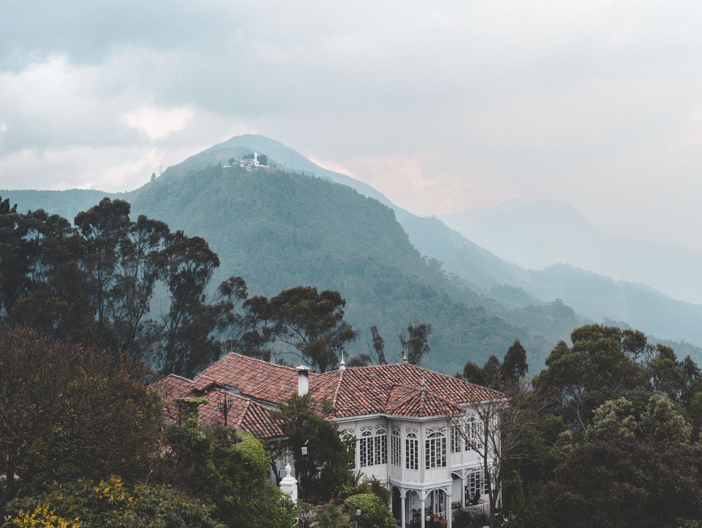 Colonial-style house nestled in misty mountain landscape.