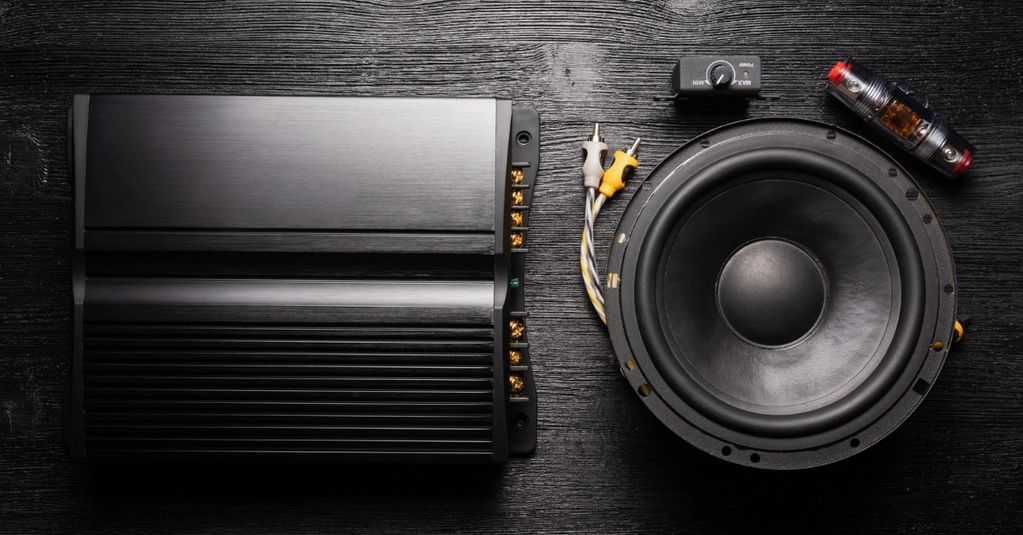 Black audio amplifier and speaker components on a dark wooden surface.