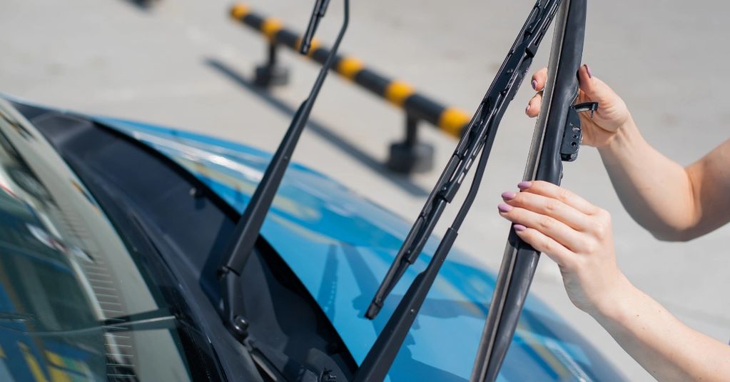 Person replacing windshield wipers on a blue car outdoors.