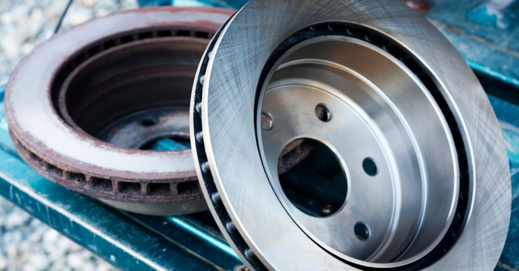 Comparison of a new and a rusty old brake disc rotor on a metal surface.