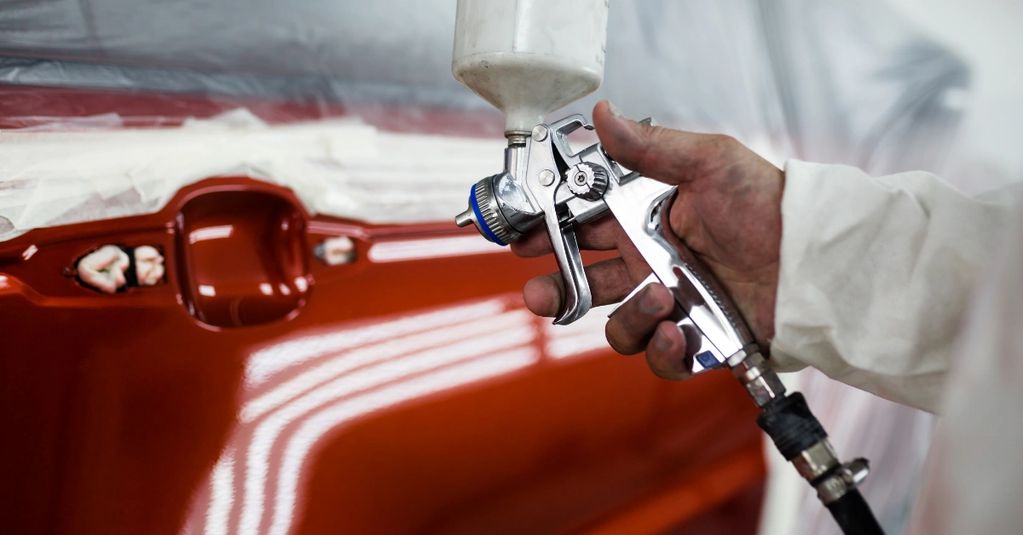 A person spray painting a car part with a glossy red finish.