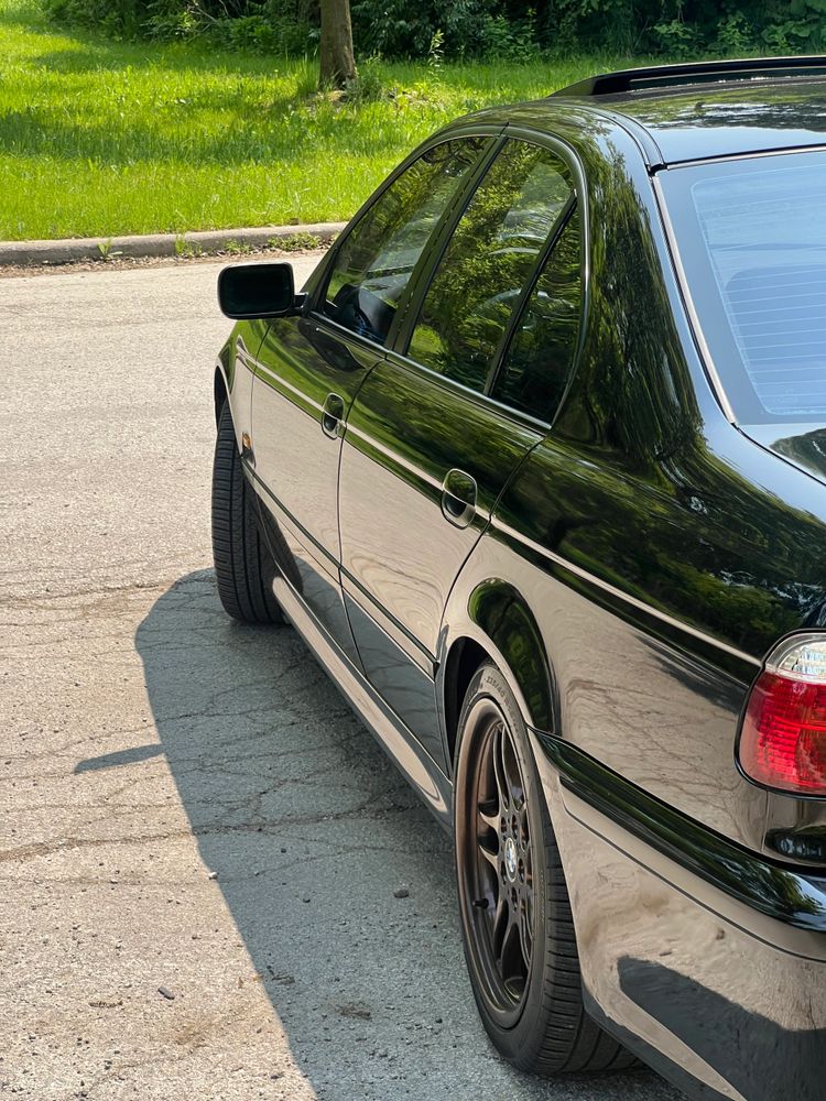 Side view of a sleek black car parked on a sunny street.