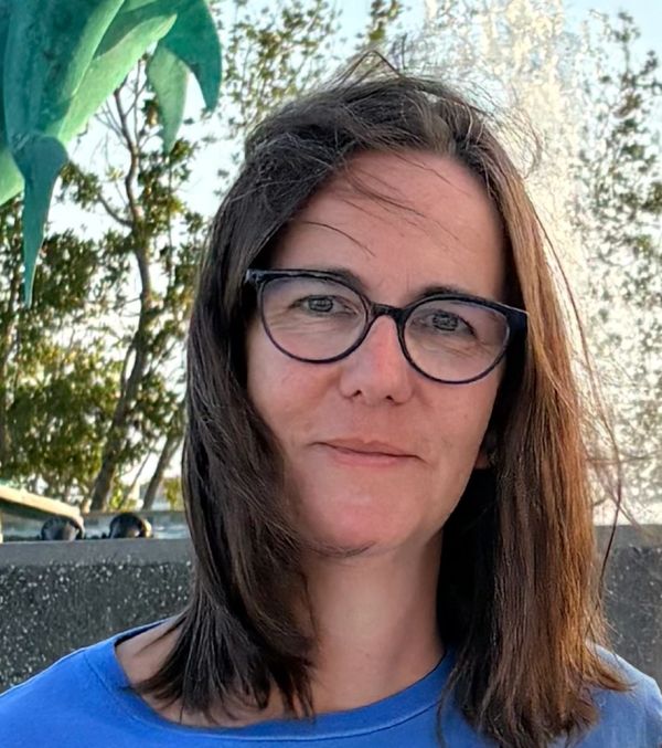 Woman with glasses and shoulder-length hair outdoors in natural light.
