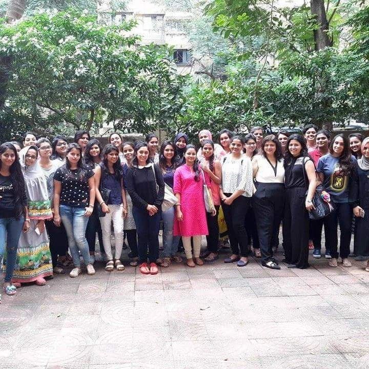 A large group of women standing together outdoors with greenery in the background.