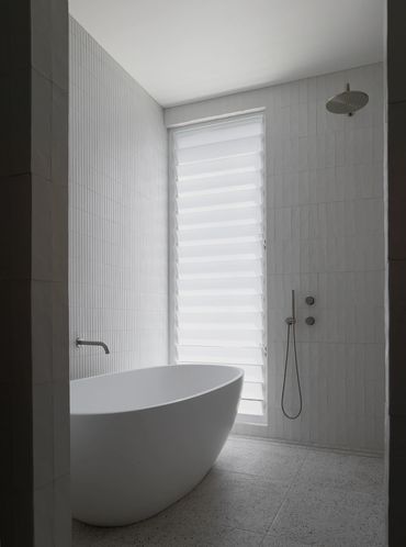 Minimalist bathroom with a sleek white bathtub and rain shower.