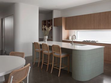 Modern kitchen with wooden cabinets and green-tiled island with bar stools.