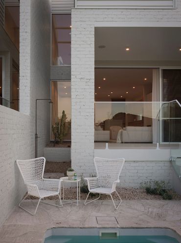 Minimalist outdoor patio with two white chairs and a small table by a pool.