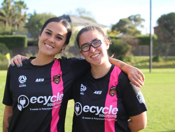 Two smiling female soccer players in black and pink uniforms.