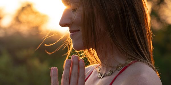 Woman meditating with hands in prayer at sunset.