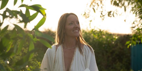 Woman in white dress smiling outdoors at sunset.