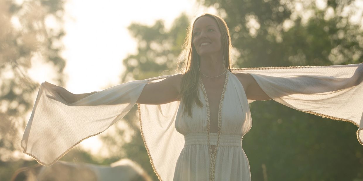 Woman in white dress with arms outstretched at sunset.