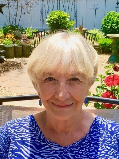Smiling older woman with short blonde hair in a garden.