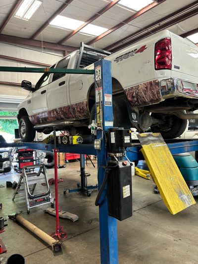 White Dodge Ram truck on a lift in a busy auto repair shop.