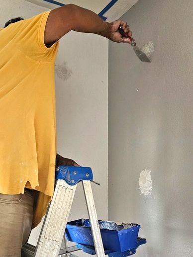 Man repairing wall with putty on stepladder.