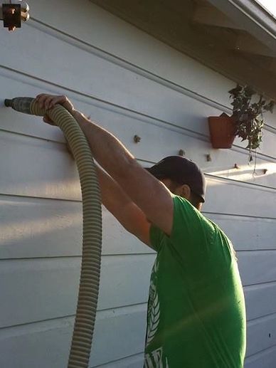 Man cleaning house exterior using a hose.