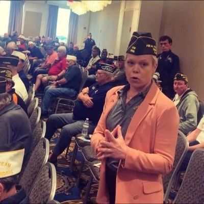 Woman in a peach blazer speaking at a veterans' meeting.