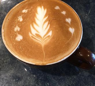 A cup of coffee with intricate latte art of a leaf and small hearts.