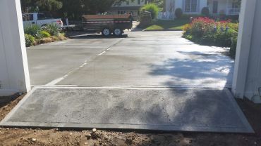 Freshly paved concrete driveway with a truck and trailer parked at the end.