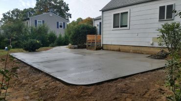 Newly poured concrete patio next to a white house.