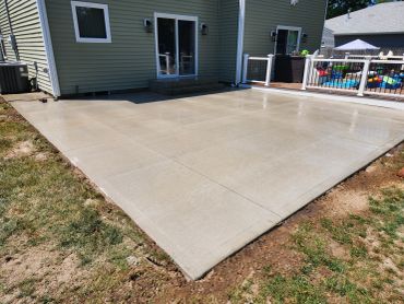 Clean concrete patio next to a house with a fenced deck.