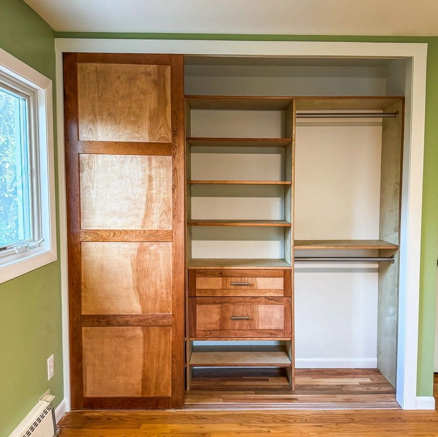 Wooden sliding door closet with shelves and drawers in a green-walled room.