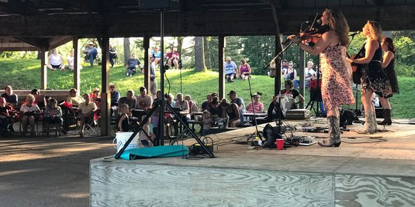 Band playing outdoors on a stage with audience seating.