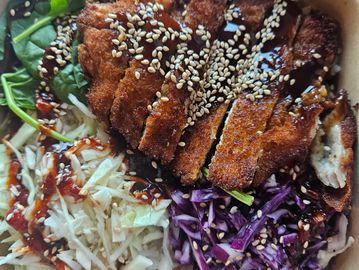Crispy breaded chicken with cabbage salad and spinach, topped with sesame seeds and sauce.