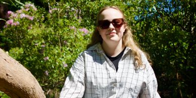 Young woman wearing sunglasses outdoors in a leafy setting.