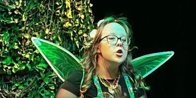 Person dressed as a fairy with green wings speaking or performing.
