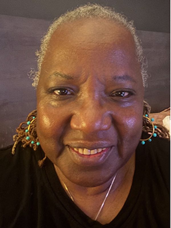 Smiling elderly woman with earrings and short curly hair.