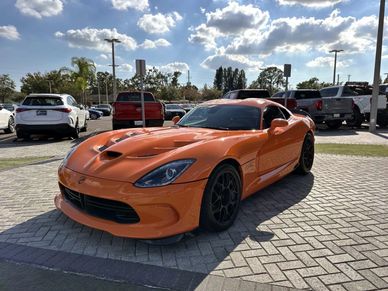 Bright orange sports car parked on a sunny day with a blue sky and clouds.