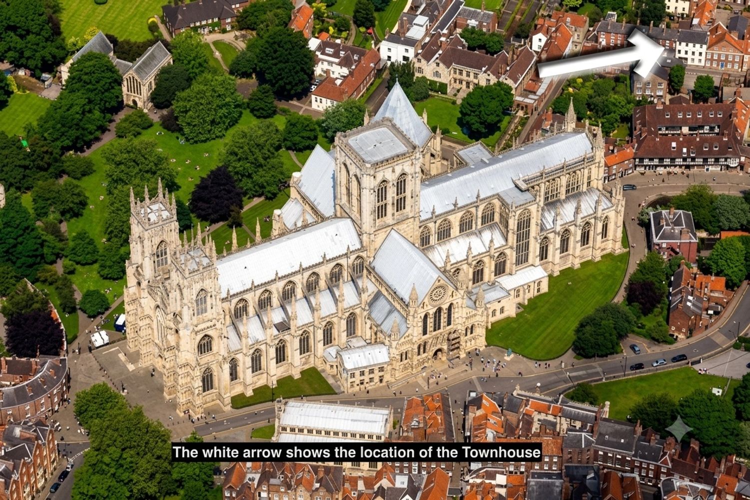 Aerial view of a large cathedral with a white arrow pointing to a townhouse.