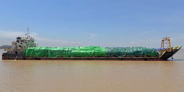 A barge covered with green tarps floating on brown water under a clear sky.
