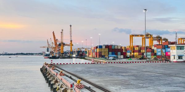 Container port with cranes and stacked cargo containers at sunset.