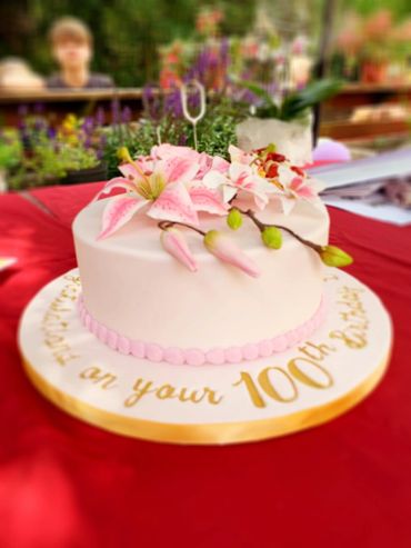 Elegant cake with pink flowers celebrating a 100th birthday.