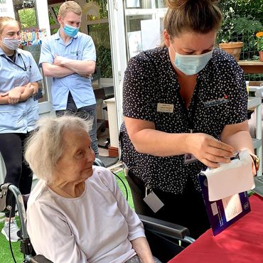 Caregiver assisting elderly woman in wheelchair during a social event.